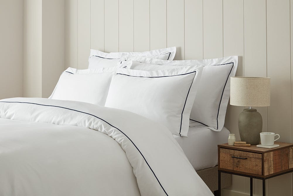 White bedding set with black piping on a bed against a neutral wall.