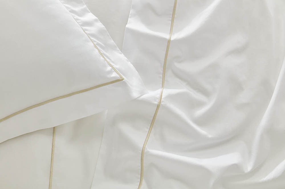Close-up image of the fitted sheet from our organic cotton bedding collection#colour_white-with-sand-trim
